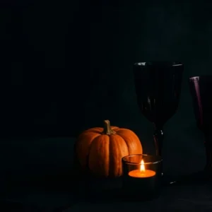 Dark-themed Halloween table setting with pumpkins, candles, and spooky glassware