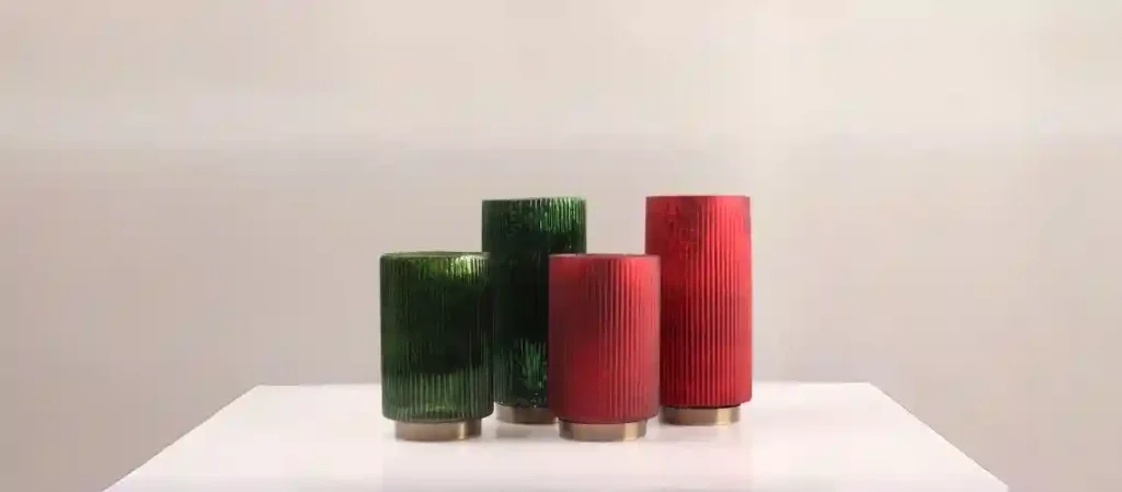 Four handcrafted ribbed mercury glass tumblers with antique gold-tone bases, displayed on a white surface: two rich emerald green on the left and two vibrant ruby red on the right, against a light gray background.