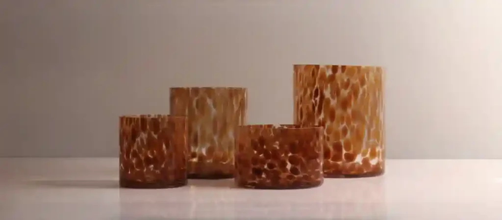 Four handmade amber tortoiseshell glass tumblers with irregular leopard-spot pattern in shades of caramel, brown, and cream, arranged by height on a white surface against a neutral backdrop.