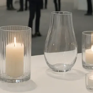 Modern glassware exhibition hall showcasing elegant glass vases and candle holders under natural light during a global trade fair.