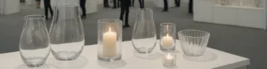 Modern glassware exhibition hall showcasing elegant glass vases and candle holders under natural light during a global trade fair.